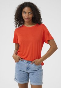 Červené tričko s krátkým rukávem a volným střihem, spárované s světle modrými džínovými šortkami s ohrnutými lemy a předními kapsami. Hladká textura.