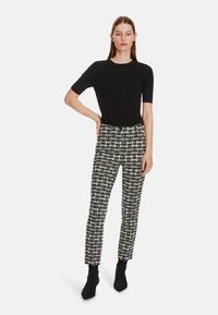 Schwarzes Kurzarmtop kombiniert mit hochgeschnittenen, gemusterten Hosen in Schwarz und Weiß mit schlanker Passform. Das Model trägt schwarze Stiefeletten.