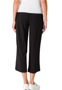 Zwarte cropped broek van zacht materiaal met een elastische tailleband, met een losse pasvorm en een rechte snit, die net boven de enkel eindigt.