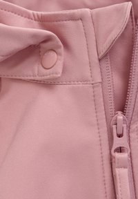 Närbild av rosa tyg som visar en tryckknapp och YKK-dragkedja, båda i matchande färg; texturen är slät med en lätt lyster.