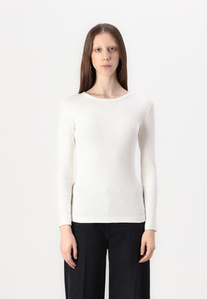 Top blanco de manga larga acanalada con cuello redondo, hecho de un material texturizado; combinado con pantalones anchos oscuros.