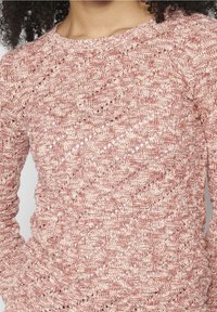 Pull tricoté rouge et crème texturé avec un col rond et des manches longues, présentant un motif complexe de mailles ajourées et de coutures.