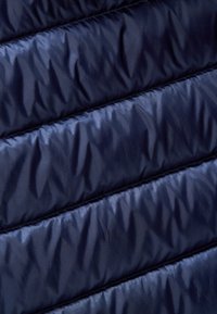 Navyblauwe gewatteerde stof met een gladde textuur, met verticale naden en een licht glanzend oppervlak. Opgeblazen secties creëren een opvallend patroon.