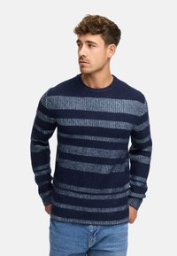 Mørkeblå sweater med horisontale striber i lys blå. Ribbet tekstur, rund hals og lange ærmer. Sammen med lys blå jeans.