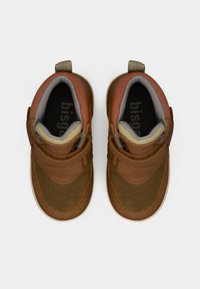 Zapatos marrones con una combinación de materiales de cuero y ante. Cierre con correa, puntera redondeada y forro gris. Detalles texturizados y suela plana de goma.