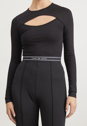 Czarny top z długim rękawem i asymetrycznym wycięciem na klatce piersiowej, zestawiony z czarnymi spodniami z wysokim stanem i paskiem z logo Tommy Jeans.