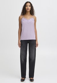 Lavendelfarbenes Spaghettiträgertop mit Spitze, dünnen Trägern, kombiniert mit locker sitzenden, dunklen Jeans und schwarzen Ballerinas. Sanfte Stofftextur, lässiges Design.