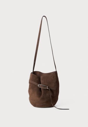 Brown suede bucket bag with a curved top, single strap, and a decorative belt detail across the body. Smooth texture, minimalist design.