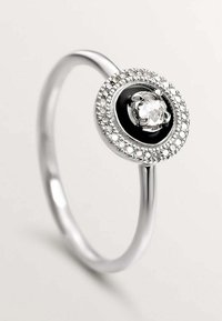 Anillo de plata con un centro redondo negro y una gema clara, rodeado de pequeños cristales claros, banda suave con acabado pulido.