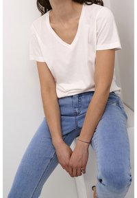 T-shirt blanc à manches courtes et col en V, fait en un mélange de coton doux, associé à un jean ajusté bleu clair. Design simple, sans motifs ni accents visibles.