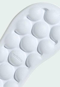 Vit texturerad innersula med runda bubbelformade mönster och präglad "adidas"-logotyp för grepp och komfort, med en slät yta.