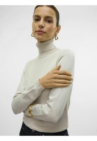 Maglione beige chiaro a collo alto con texture a coste, maniche lunghe e design aderente, abbinato a un bracciale rigido dorato.