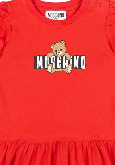 Robe rouge pour bébé avec un motif d'ourson et le texte "MOSCHINO" sur la poitrine, dotée de pressions aux épaules et d'un ourlet à volants.