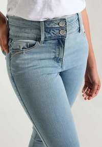 Jeans de tiro alto en azul claro, fabricados en denim, con una textura suave, cierre de dos botones y costuras sutiles en los bolsillos.
