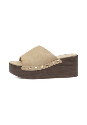 Sandalia beige de ante con punta abierta, tachuelas doradas en la parte superior y suela de cuña gruesa en plataforma marrón oscuro.