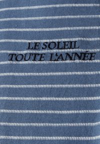 Modrá pruhovaná látka má střídající se bílé pruhy. Text "LE SOLEIL TOUTE L'ANNÉE" vyšívaný tmavě modrou barvou, umístěný uprostřed pruhů.