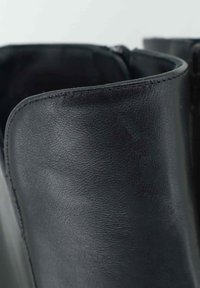 Stivaletti alla caviglia in pelle nera con una texture liscia e un bordo superiore arrotondato, cuciture visibili e chiusura con zip.