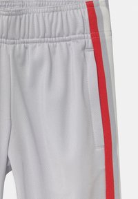 Light gray athletic pants with a textured finish, featuring red and gray side stripes and an elastic waistband for comfort.