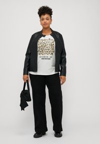 Black faux leather jacket, white shirt with animal print and text, relaxed black pants, black bag with bow detail, black boots.
