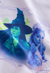 Grafisk T-krekls ar zilu un zaļu printu, uz kura attēlotas divas varones: ragana ar cepuri un princese ar kroni, uz baltas fona.