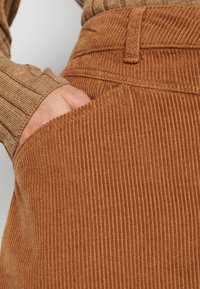 Bruine corduroy stof met verticale strepen. Close-up van een zak, die de textuur en stiksels laat zien.