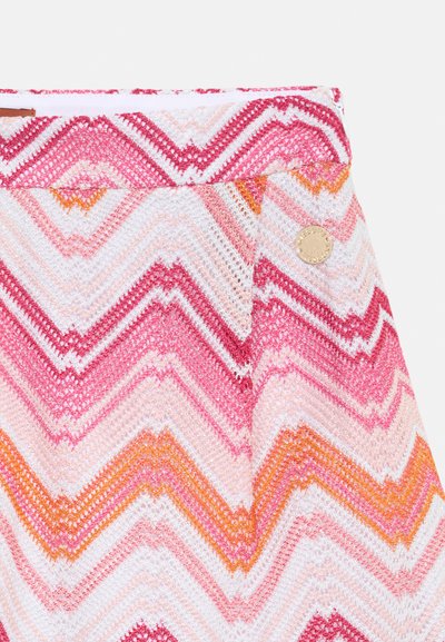 Mønstret stoff med chevron-striper i rosa, rød, oransje og hvit. Inkluderer en rund metallaccent på midjebåndet.