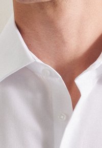 Vit krag skjorta med en klassisk knäppning, tillverkad av ett mjukt tyg med en subtil lyster och en ren, strukturerad krage.