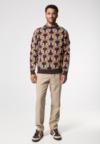 Maglione a maglia con un motivo a foglia multicolore su sfondo scuro, abbinato a pantaloni chiari e sneakers con motivo.