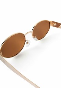 Sleek sunglasses with oval brown tinted lenses and thin gold metal frames, featuring transparent nose pads on a white background.