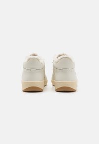 Zapatillas blancas de cuero con una suela texturizada beige y un forro blanco suave. El diseño presenta una silueta de media caña y detalles de costura sutiles.