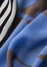 Primer plano de una tela suave con patrones geométricos en azul y marrón, junto a franjas crema y negras.