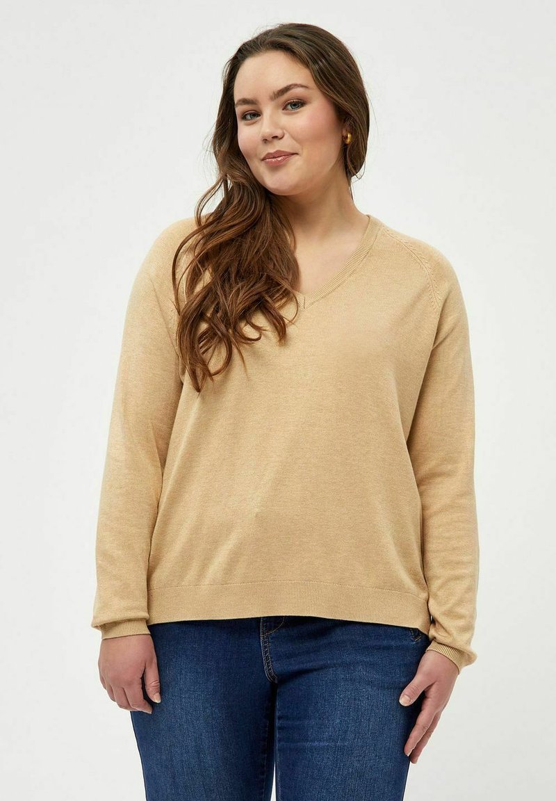 Maglione beige a maniche lunghe e scollo a V in morbido tessuto lavorato a maglia. Presenta polsini e orlo a coste, abbinato a jeans blu scuro.