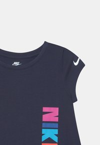 Tmavě modré tričko Nike s růžovým, modrým a oranžovým vertikálním textem "NIKE" vpředu a bílým logem Nike na levém rukávu.
