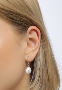 Silver hoopsmycke med en strukturerad, oregelbundet formad vit berlock. Berlocken har en slät, matt yta och hänger något nedanför hängsmycket.
