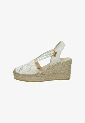 Sandalo espadrille bianco con zeppa, suola in juta intrecciata, copertura in pizzo per le dita, cinturini elastici e cinturino sul tallone in pelle con una piccola etichetta marrone.