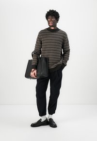 Maglione lavorato a maglia di colore marrone scuro con motivo a righe, pantaloni neri affusolati e borsa nera. Scarpe nere e calzini bianchi completano il look.