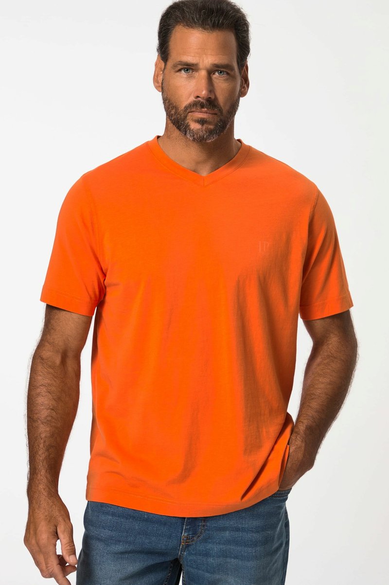 T-shirt orange à col en V en tissu doux avec des manches courtes. Présente un logo subtil à l'avant, associé à un jean en denim bleu.