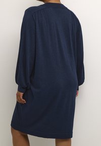 Robe pull bleu marine en tissu texturé. Possède de longues manches volumineuses, un col rond et une coupe ample et décontractée.