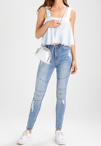 Ljusblå kort topp med fransade kanter; ljusblå skinny jeans med slitna områden och strukturerade paneler; silverfärgad axelväska.