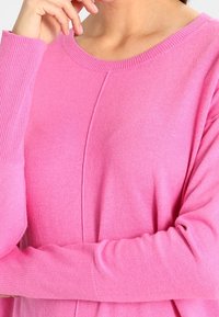 Roze trui van zachte gebreide stof, met een ronde halslijn en geribde manchetten. Naaddetail loopt verticaal over de voorkant.