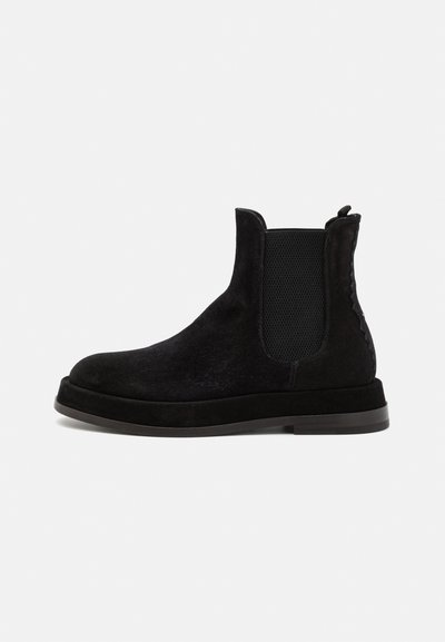 Zwarte suède Chelsea boots met elastische zijkanten, ronde neus en een vlakke zool. Textuurdetails langs de zijkant voegen visuele interesse toe.