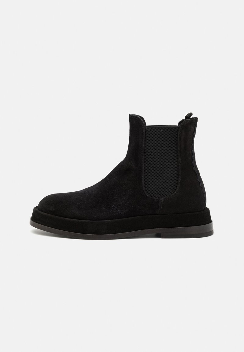 Botine Chelsea din suede negru, cu panouri elastice laterale, bot rotund și talpă plată. Detaliul texturat de-a lungul laturii adaugă interes vizual.