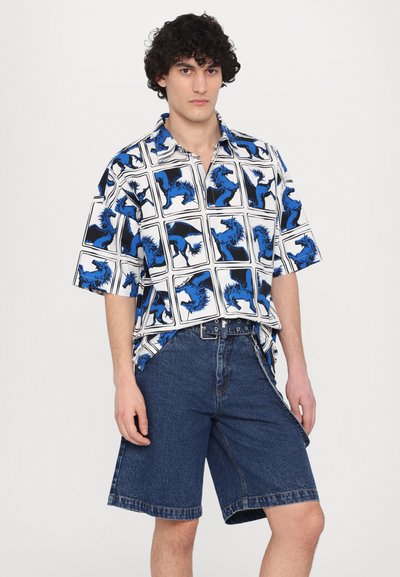 Cămașă cu mânecă scurtă cu un model grafic de cai alb-albastru, asortată cu șorturi din denim închise la culoare. Materialul pare ușor și are o croială lejeră.