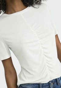 Camiseta blanca de manga corta con un diseño gathered en el lateral, hecha de una tela suave y ligera. Combinada con denim.