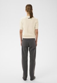 Pleteni krem pulover kratkih rukava i sivo široke hlače s stražnjim džepovima. Meka tekstura i strukirana detalj. Minimalistički dizajn.