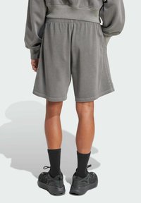 Gray cotton shorts with an elastic waistband, mid-thigh length, and side pockets. Worn with black socks and athletic shoes, viewed from behind.