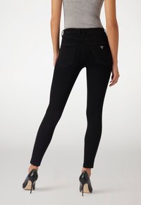 Jeans negros ajustados con una cintura alta, bolsillos traseros y un pequeño detalle de logo triangular cerca del bolsillo derecho. Textura suave.