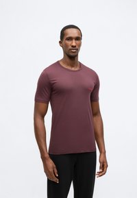 Burgundské tričko s krátkým rukávem a kulatým výstřihem, s červeným logem na hrudi. Látka je hladká a elastická.