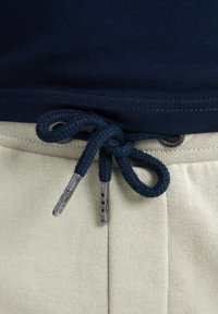 Marineblauwe katoenen T-shirt in de lichte beige katoenen joggingbroek gestoken, met marineblauwe trekkoorden met metalen uiteinden en een gestructureerde tailleband.