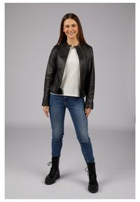 Black leather jacket with a round neckline, fitted shape, and zip closure, paired with a white shirt and blue jeans, finished with black combat boots.